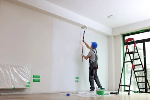 Painter rolling a bright white wall in an empty room with plastic-covered furniture