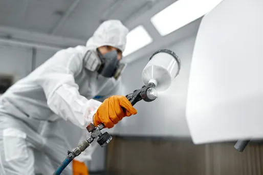 Painter in protective suit and respirator spraying a smooth finish