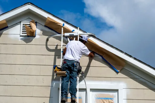 Painter on a ladder masking and painting lap siding near a gable